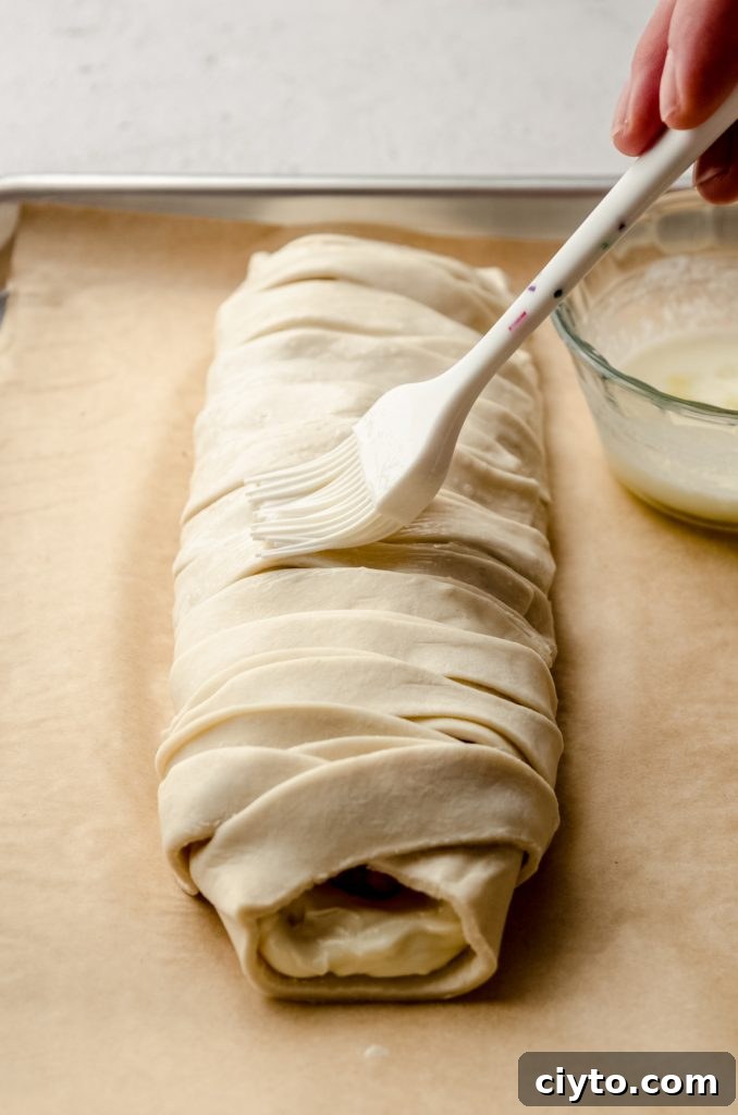 Raspberry Cream Cheese Danish Recipe 13 Someone is brushing a pastry braid with an egg wash.