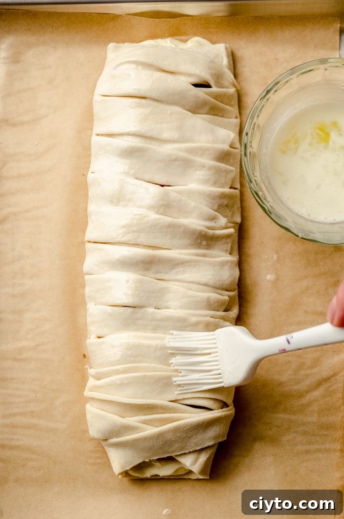 Raspberry Cream Cheese Danish Recipe 14 Someone is brushing a pastry braid with an egg wash.