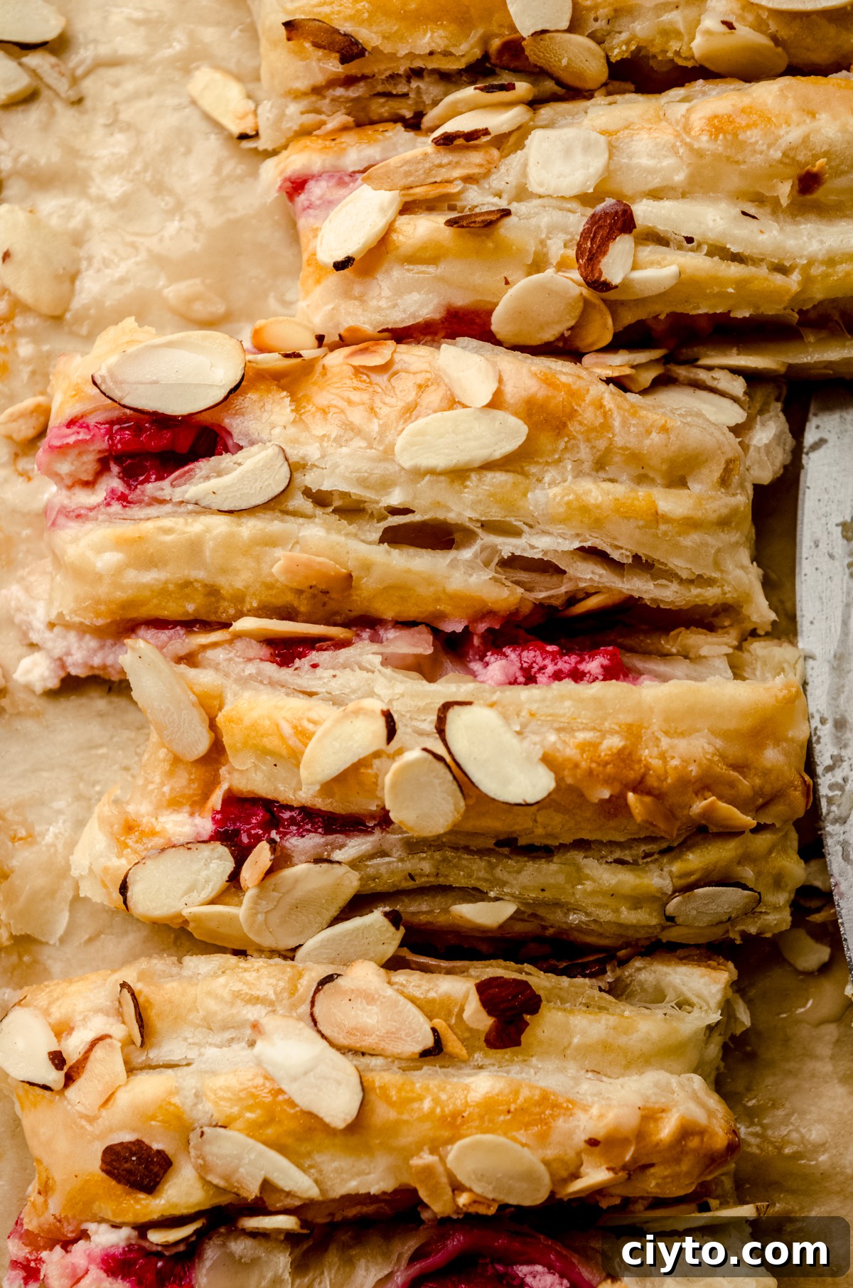Raspberry Cream Cheese Danish Recipe 3 A pastry braid filled with raspberries and cream cheese with toasted almonds and an icing on it sliced into portions.
