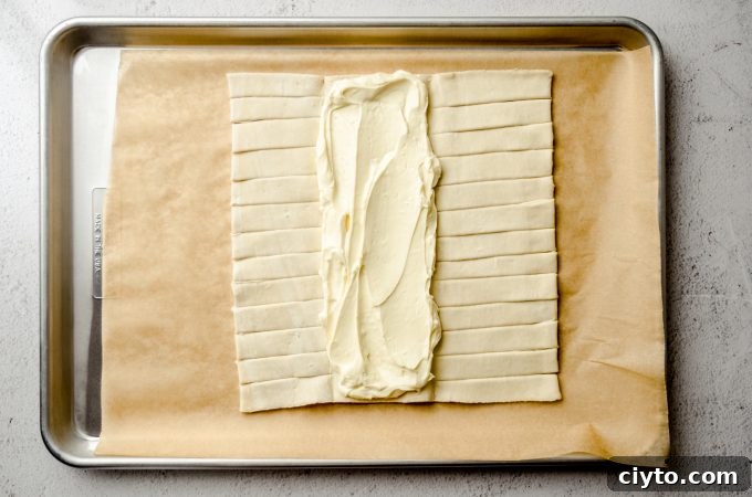 Raspberry Cream Cheese Danish Recipe 9 A rectangle of puff pastry dough on a baking sheet lined with parchment paper with cream cheese filling on the center flap.