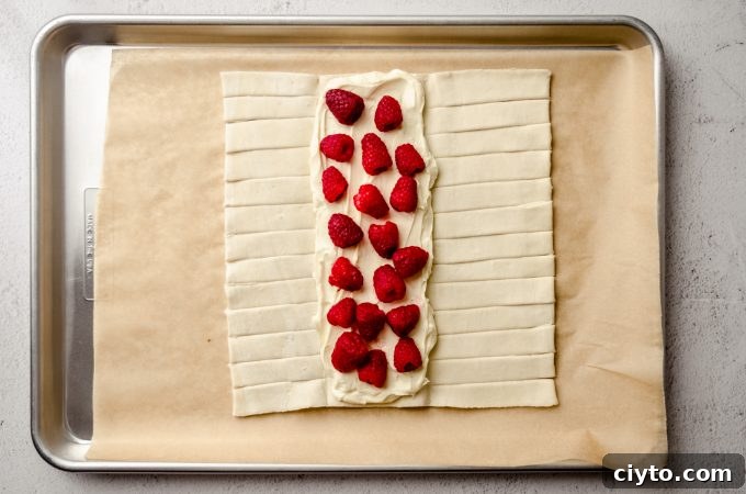 Raspberry Cream Cheese Danish Recipe 10 A rectangle of puff pastry dough on a baking sheet lined with parchment paper with cream cheese filling and fresh raspberries on the center flap.