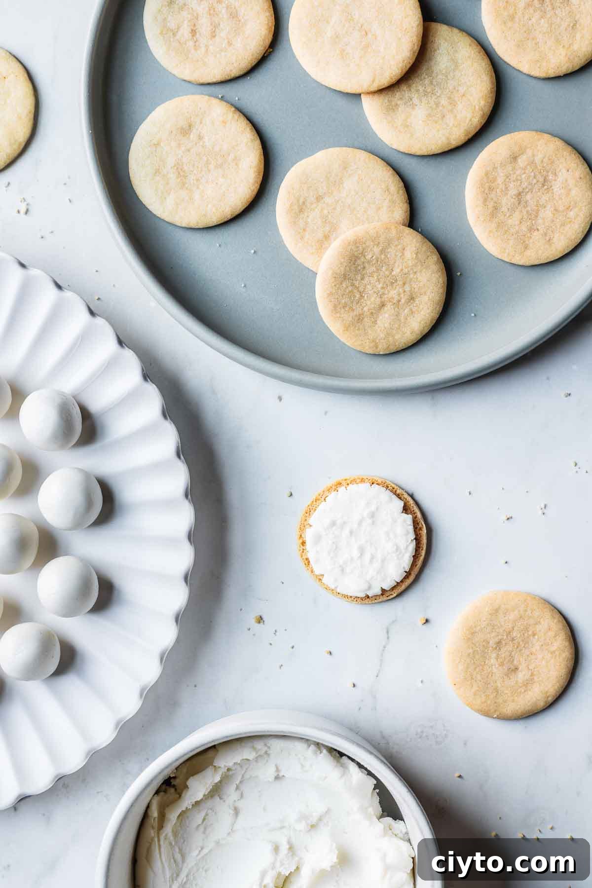 Round vanilla cookies and scoops of vanilla creme filling on plates ready to be sandwiched together.