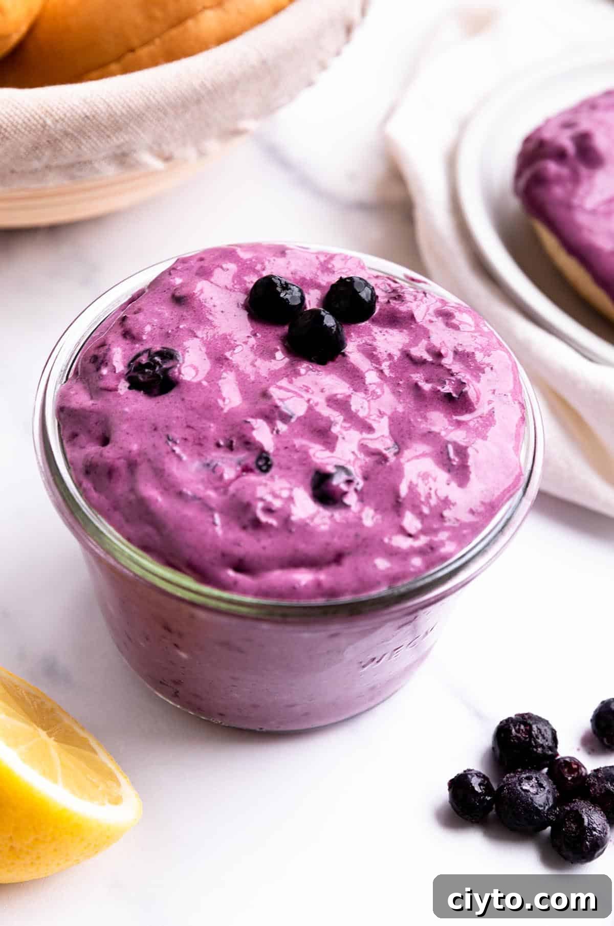 A jar of blueberry cream cheese with a fresh lemon and basket of bagels.