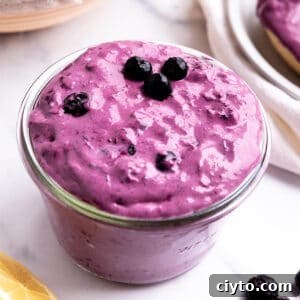 A jar of purple cream cheese with fresh blueberries on top.