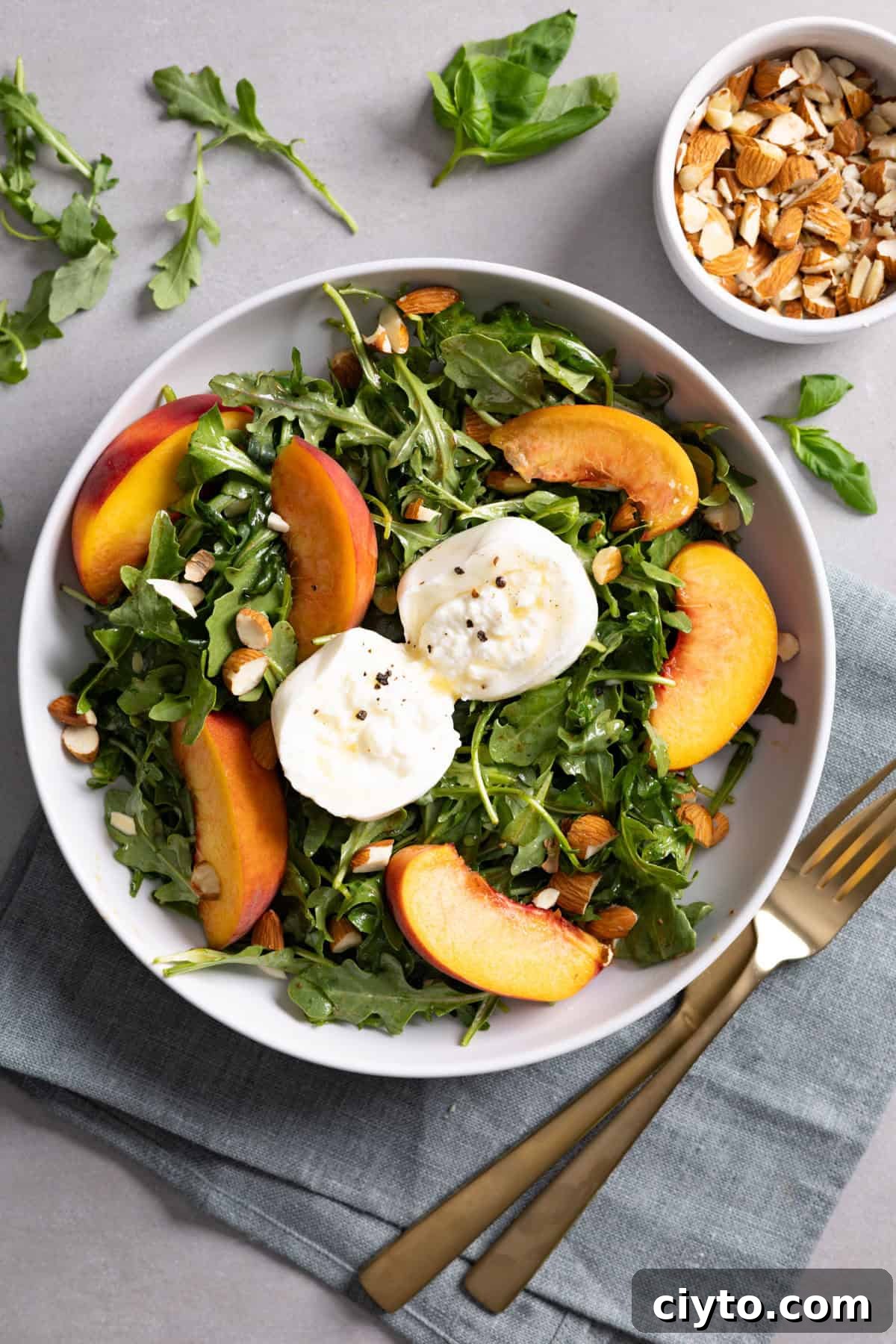 Arugula and Burrata Salad Recipe with Lemon Vinaigrette 2 A bowl of arugula burrata salad with peaches and almonds.