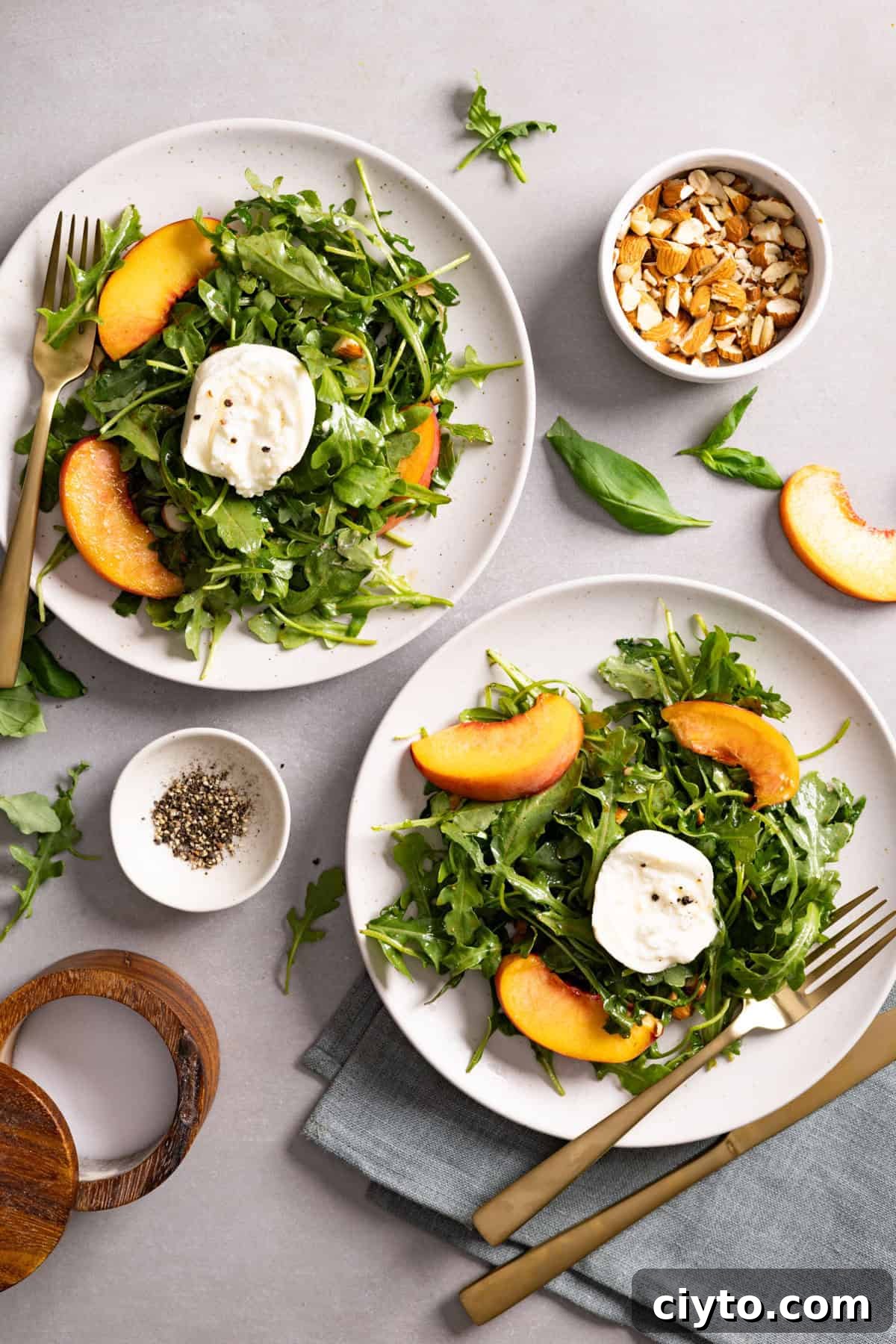 Arugula and Burrata Salad Recipe with Lemon Vinaigrette 12 Two plates of arugula burrata salad topped with peaches and almonds.
