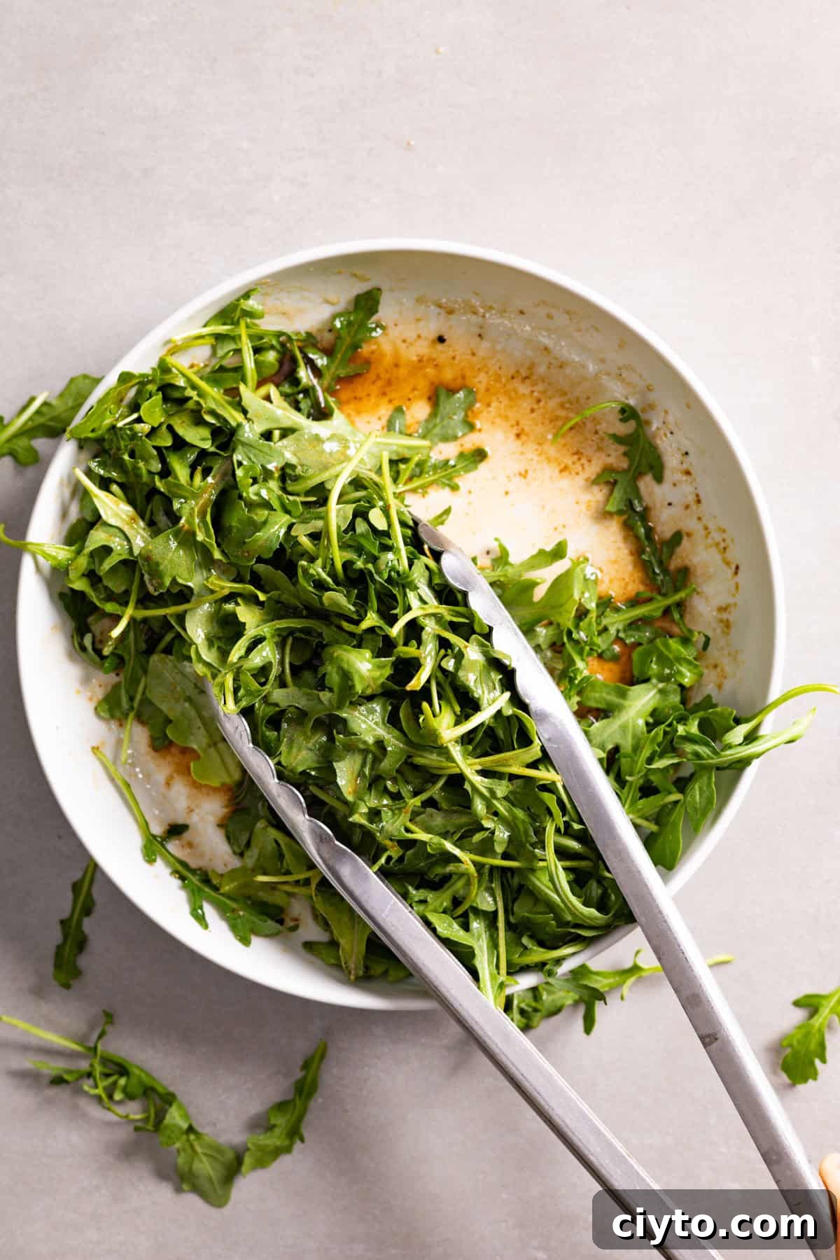 Arugula and Burrata Salad Recipe with Lemon Vinaigrette 8 Arugula getting tossed in a bowl with balsamic vinaigrette.