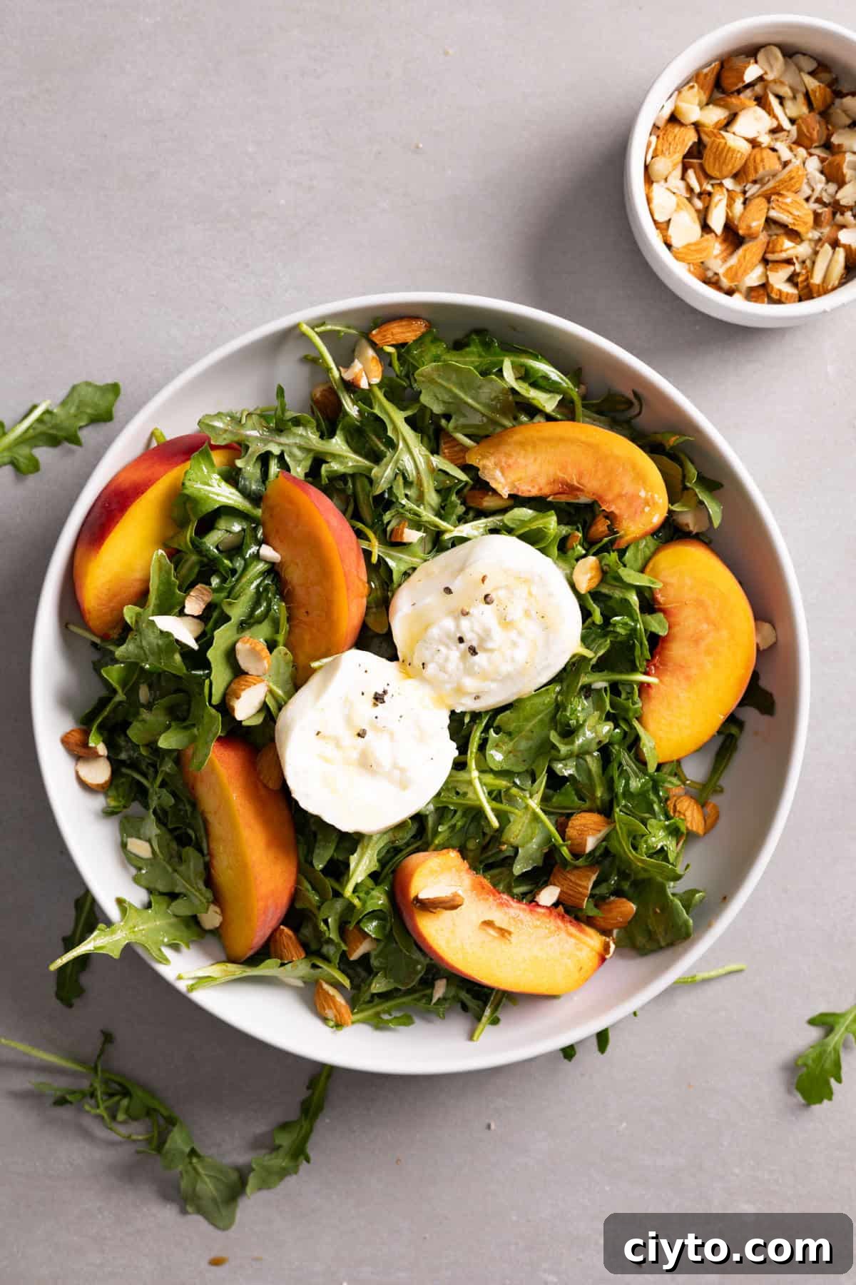 Arugula and Burrata Salad Recipe with Lemon Vinaigrette 9 Arugula burrata salad in a bowl topped with peaches and almonds.