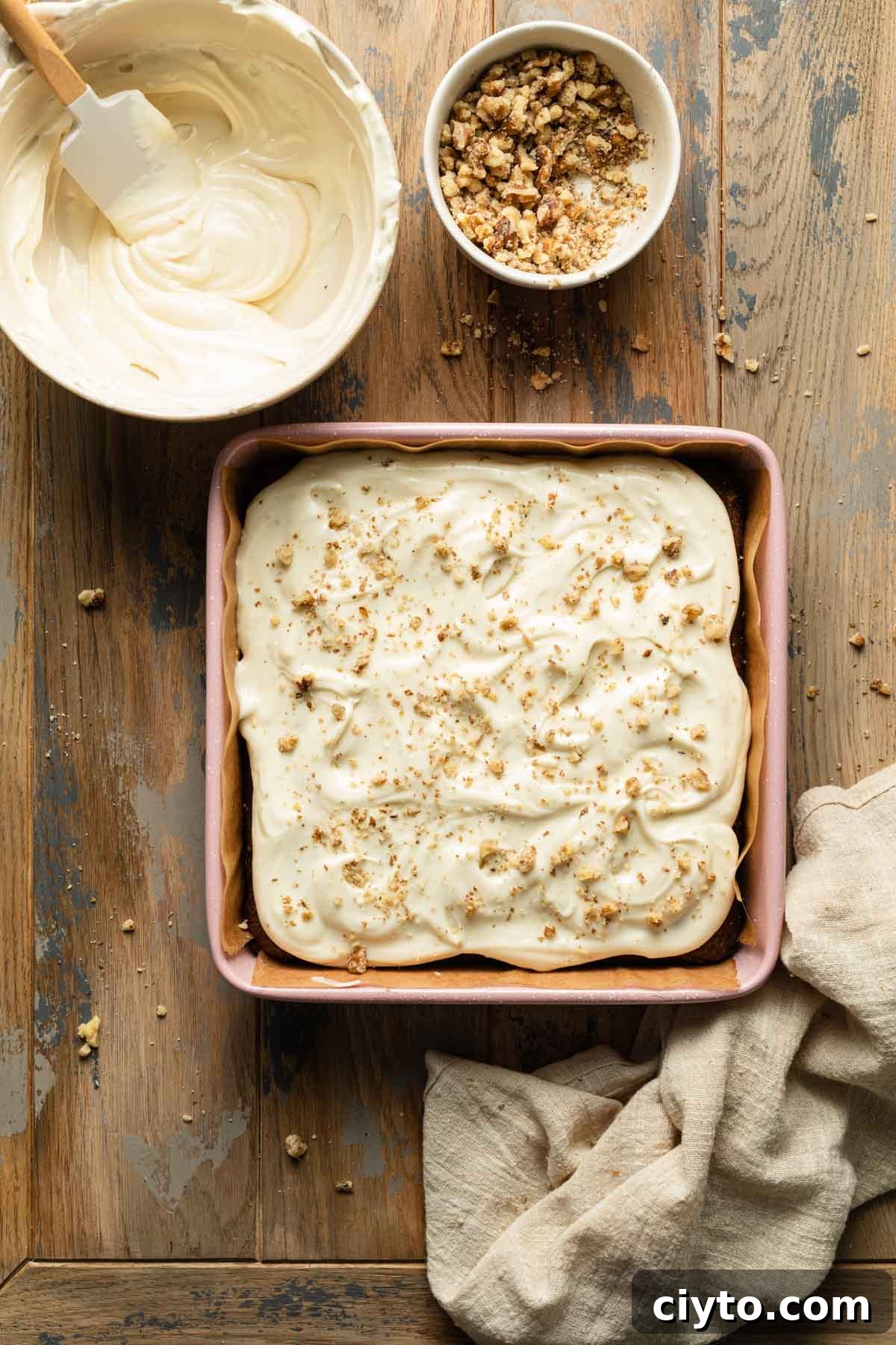 Small carrot cake in a square pan topped with cream cheese frosting and walnuts.