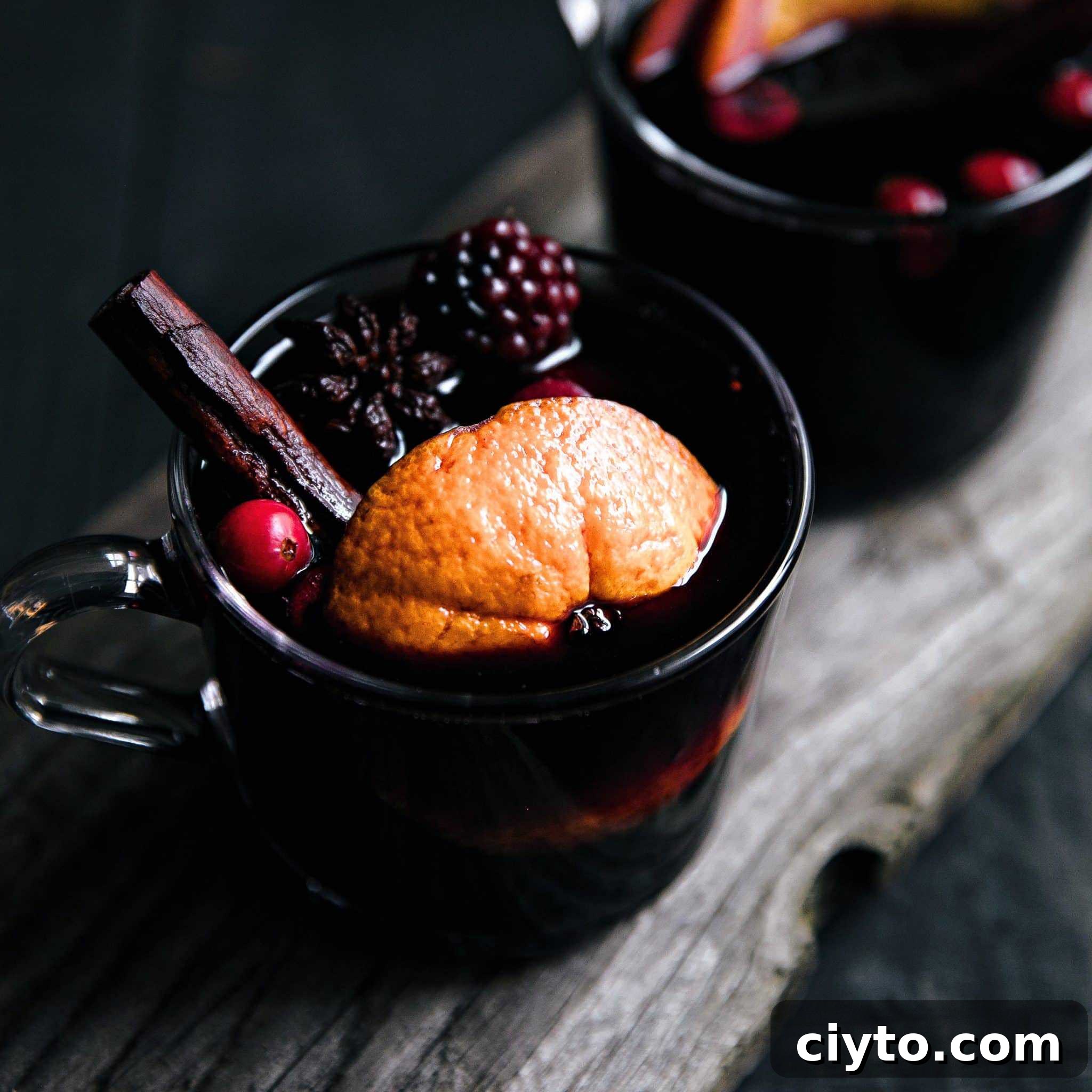 A mug of mulled wine with berries and a cinnamon stick.