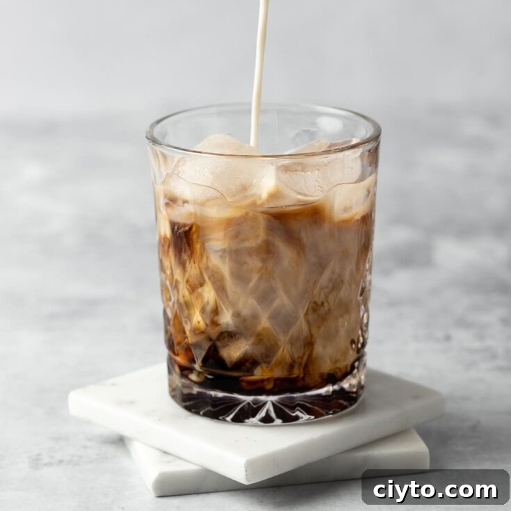 RumChata being poured into a rumchata white russian cocktail, on a white background.