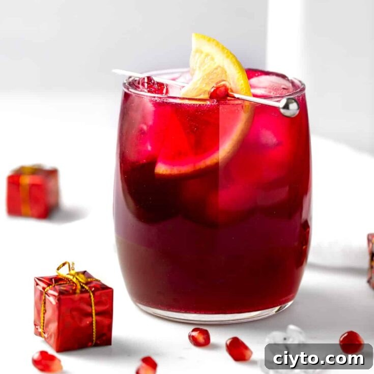 A pomegranate gin cocktail garnished with a lemon slice on a white marble table.