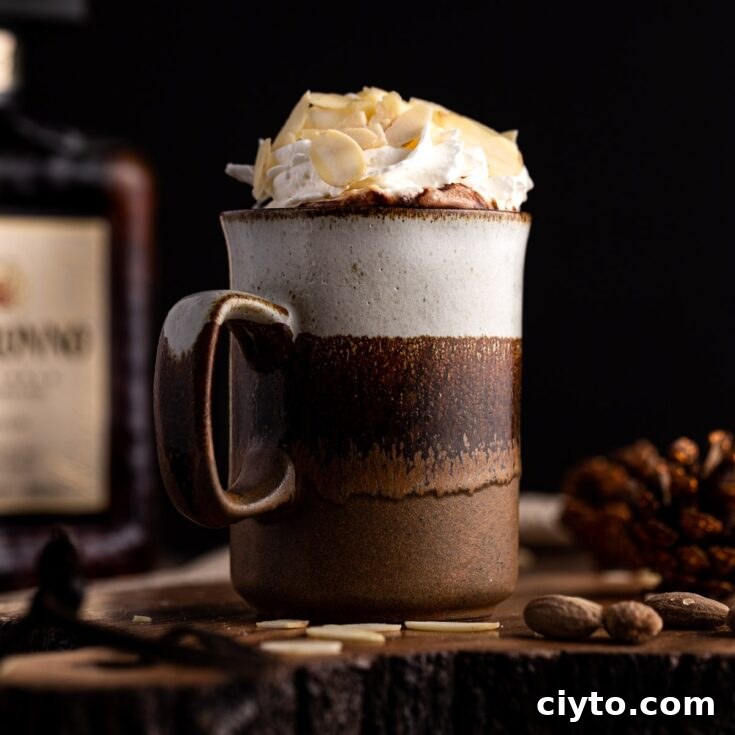 Side view of a brown mug of dark hot chocolate with amaretto, topped with whipped cream and sliced almonds, in front of a black background.
