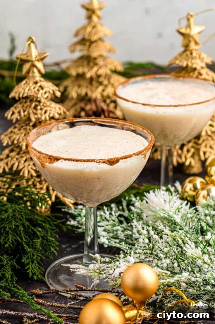 A couple eggnog martinis with a cinnamon rim and Christmas trees in the background.