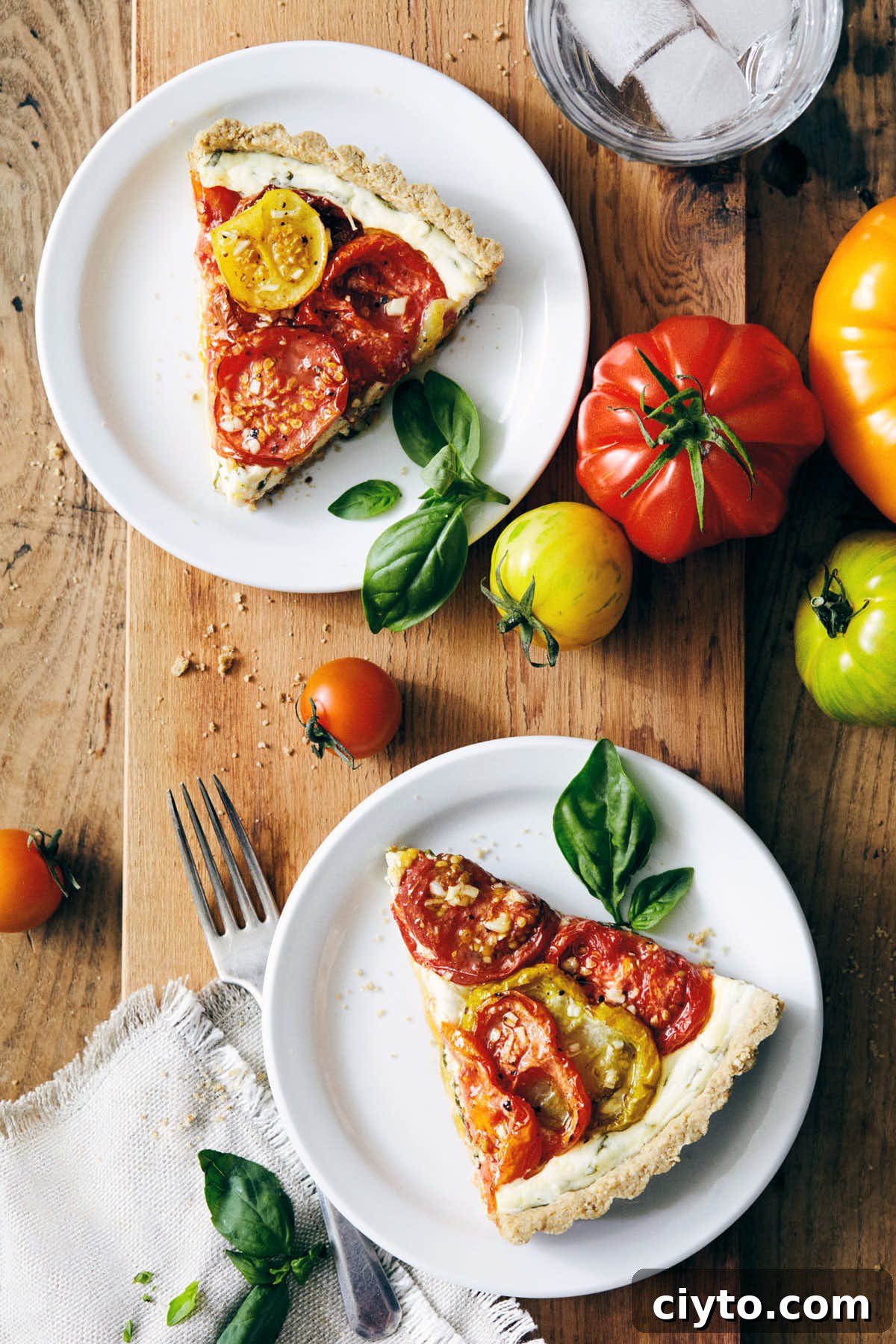 Two pieces of heirloom tomato tart on a serving board with heirloom tomatoes