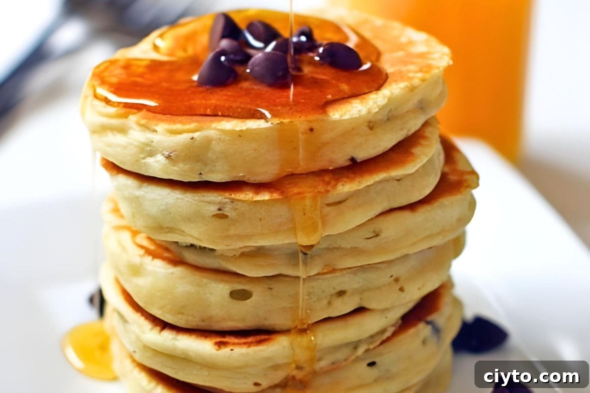 A stack of fluffy chocolate chip pancakes with maple syrup drizzled on them.