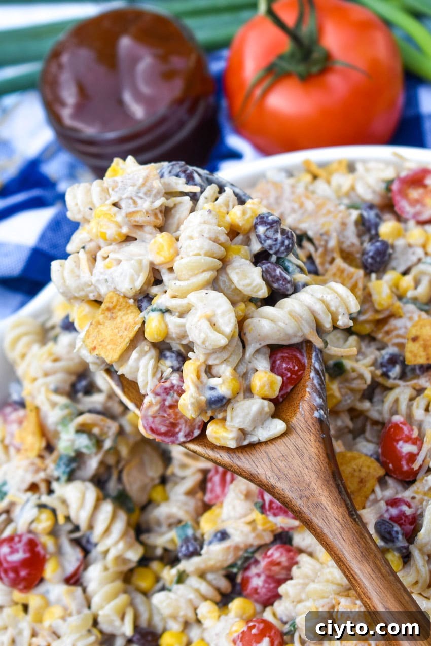 a wooden spoon holding up a scoop of barbecue chicken pasta salad