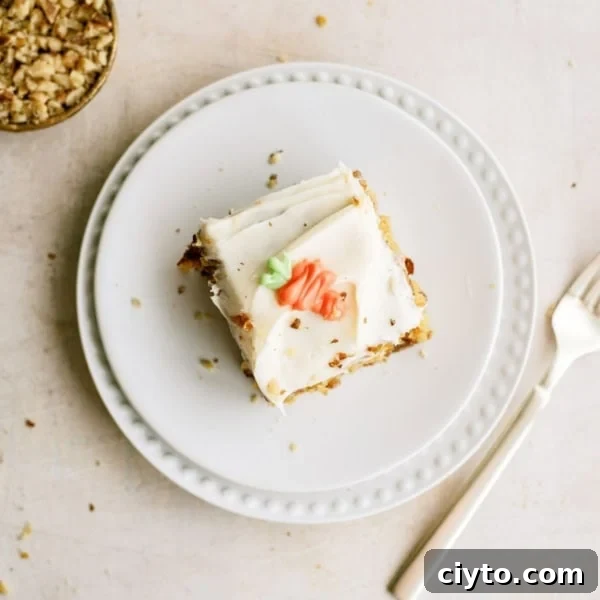 A slice of frosted cake with decorative icing sits on a white plate next to a fork; a small bowl of chopped nuts is nearby.