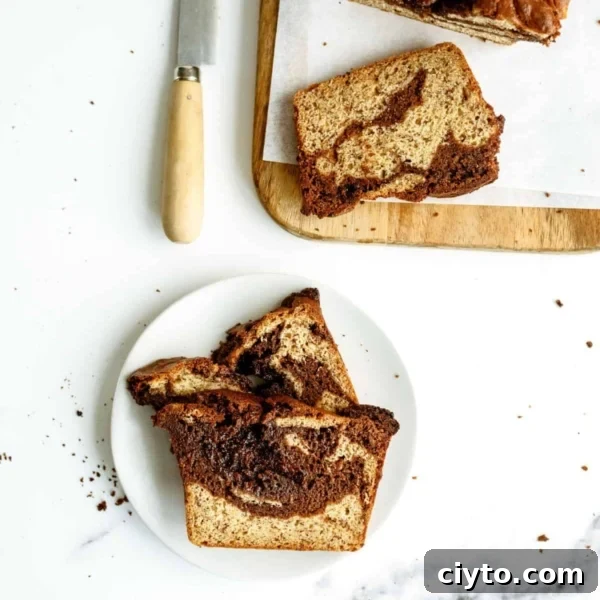 Two slices of a marbled loaf cake on a white plate, with more slices and a knife on a wooden cutting board nearby. Crumbs are scattered on the white surface.