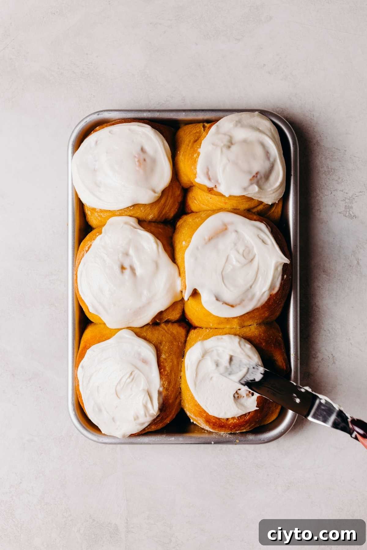 Maple frosting being spread onto pumpkin cinnamon rolls.