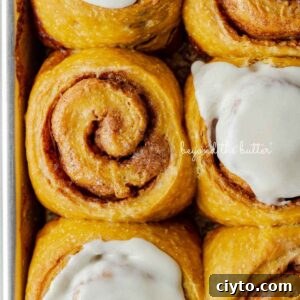 Six pumpkin cinnamon rolls with three topped with maple frosting placed on a small baking sheet.