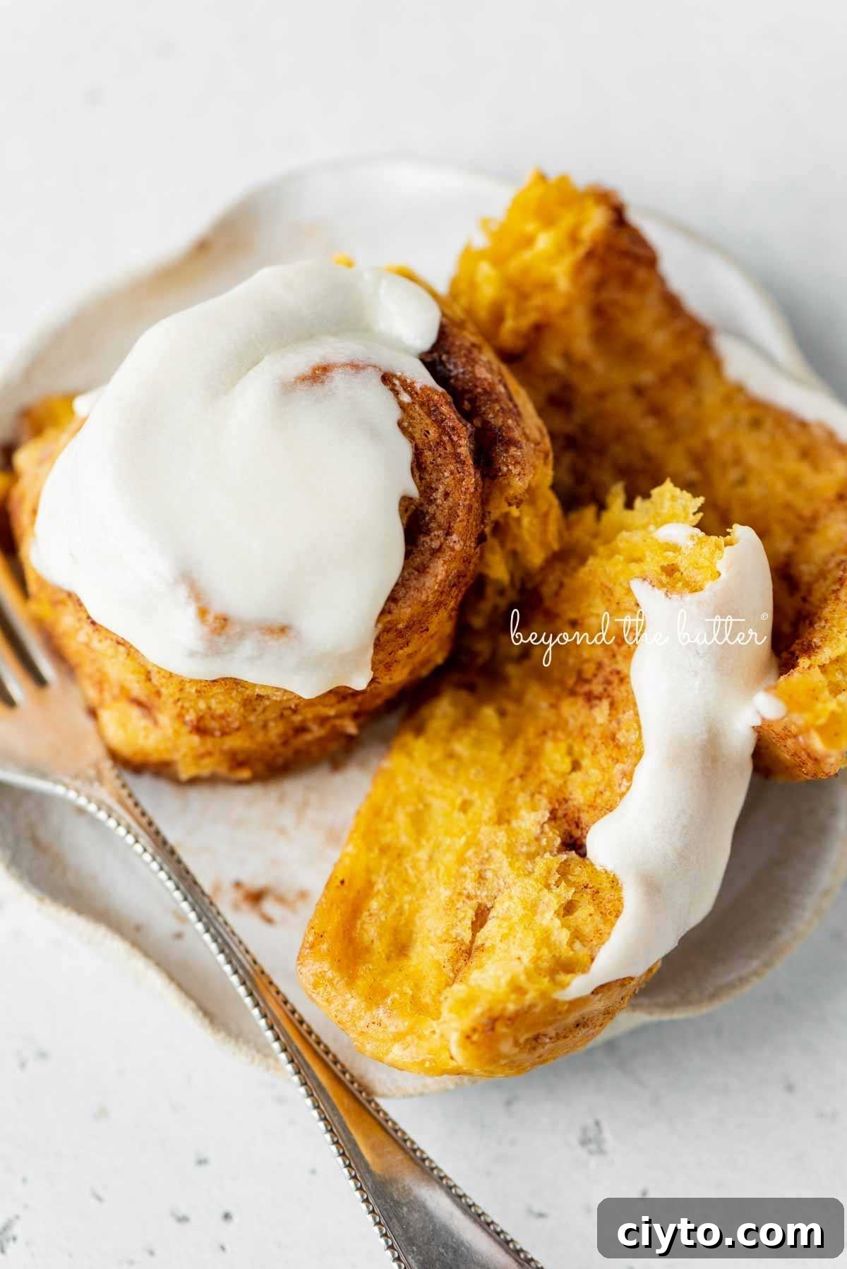 Unraveled, half eaten pumpkin cinnamon roll on a dessert plate with small fork on a white marbled background.