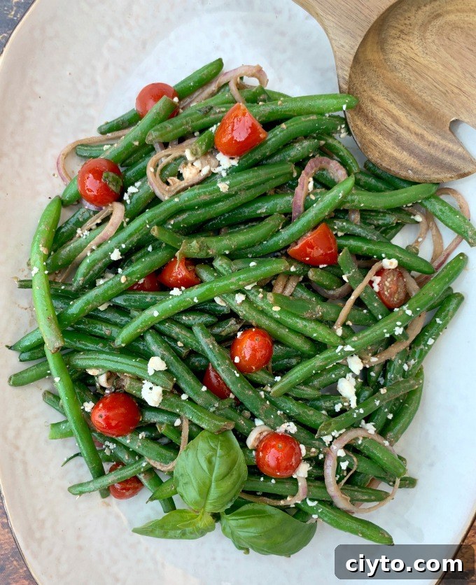 cold green bean salad with tomatoes and feta cheese on a white plate