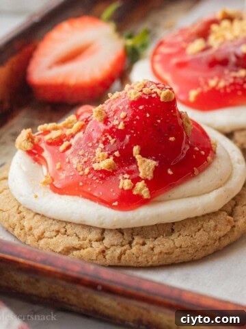 Baked strawberry cheesecake cookie on baking sheet with fresh strawberry.