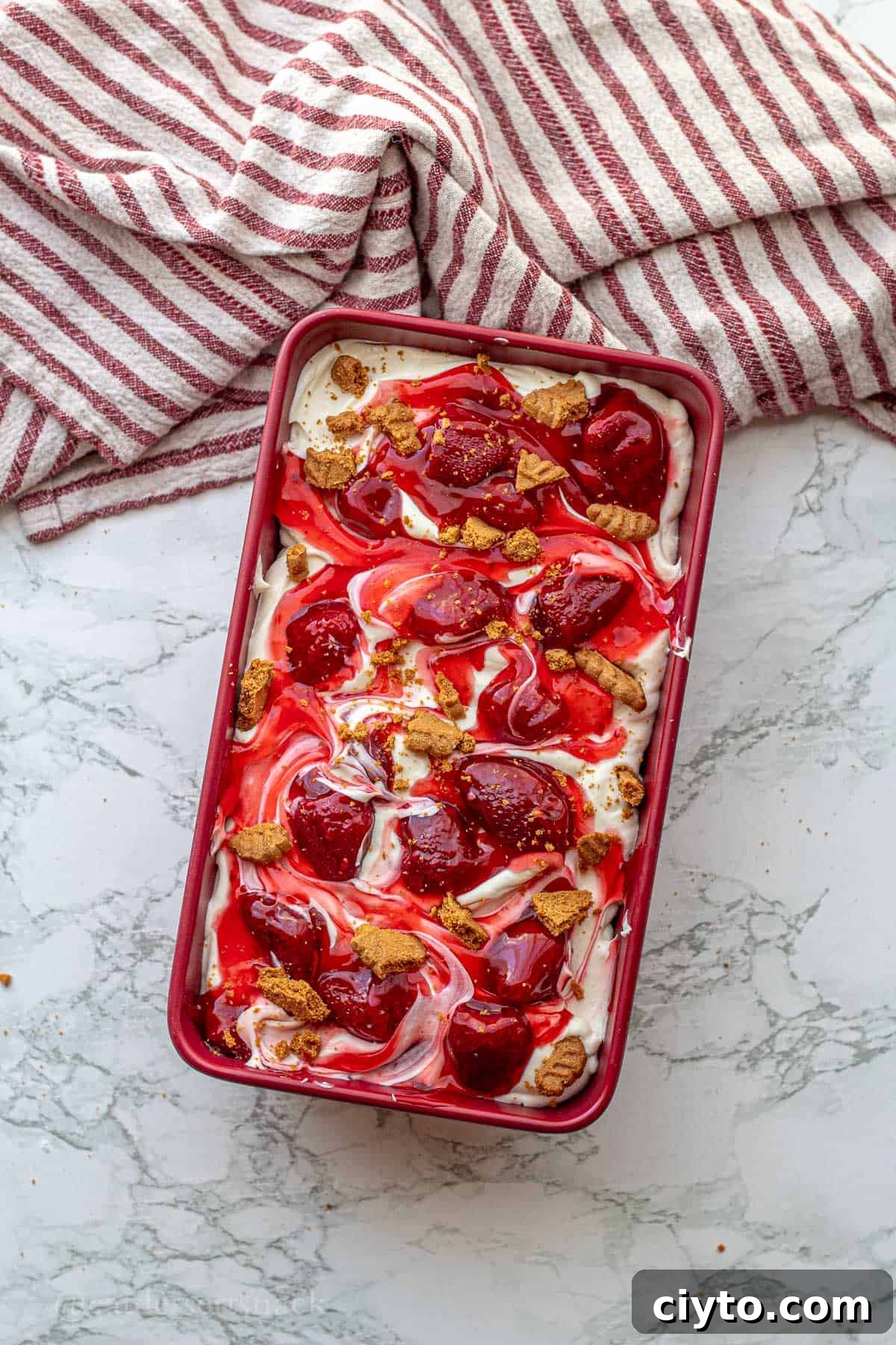 Strawberry cheesecake ice cream in a pan with biscoff crumbles on top.