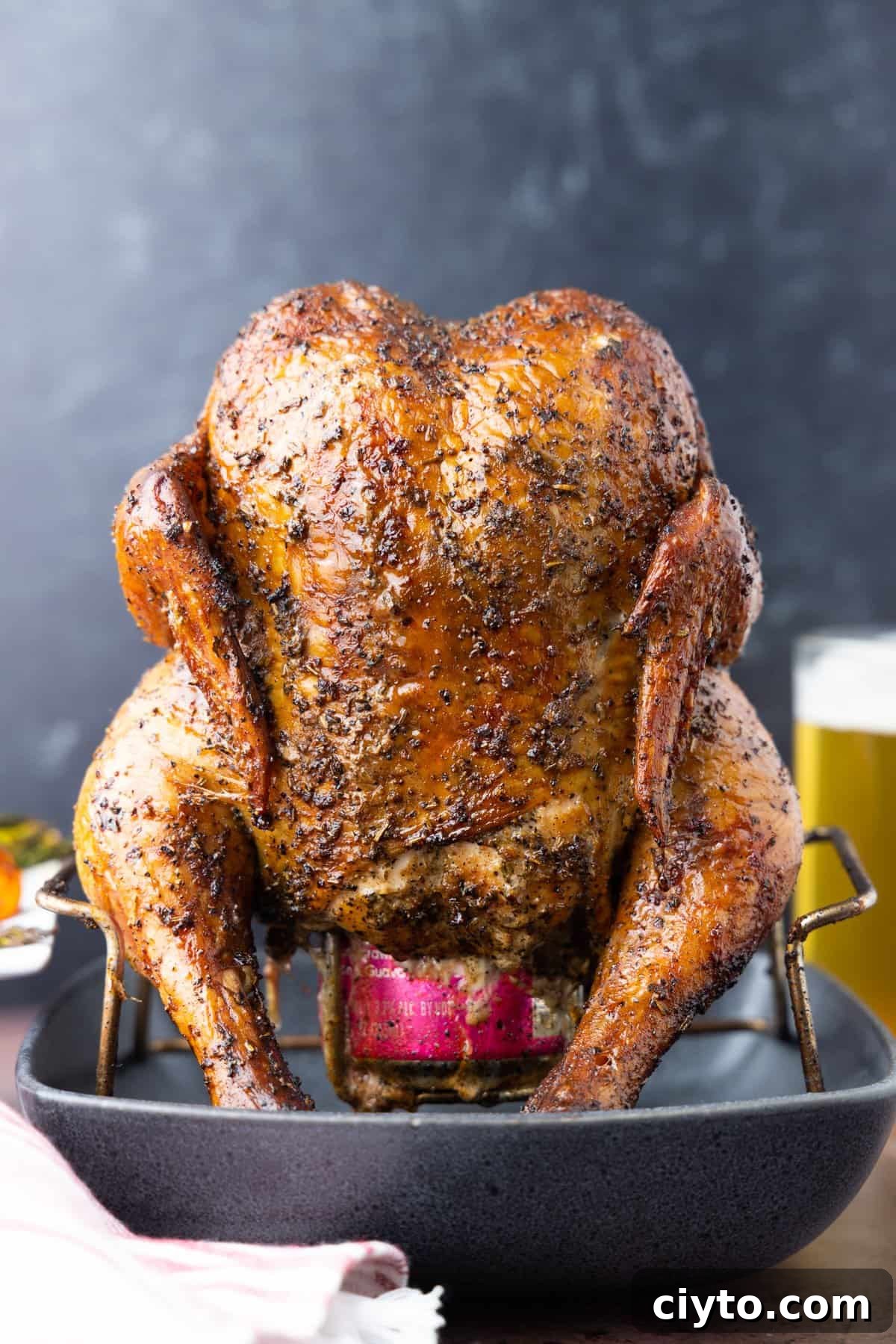 How to Smoke Beer Can Chicken 2 Beer can chicken on rack with black background and beer in glass