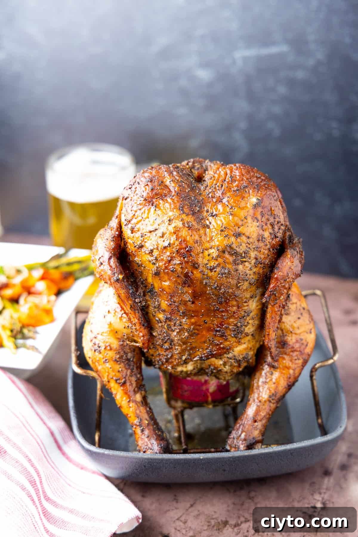 How to Smoke Beer Can Chicken 11 Chicken on beer can with black background and beer in glass.
