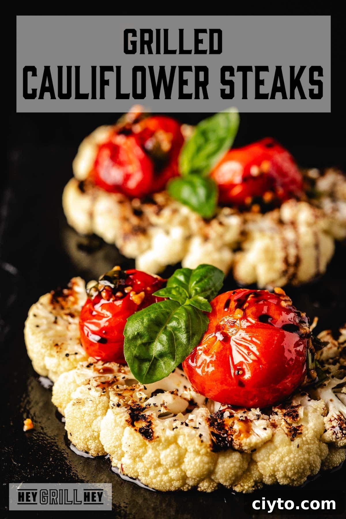 Grilled cauliflower topped with tomato and basil. The text overlay at the top reads 'Grilled Cauliflower Steaks,' and at the bottom it reads 'Hey Grill Hey.'