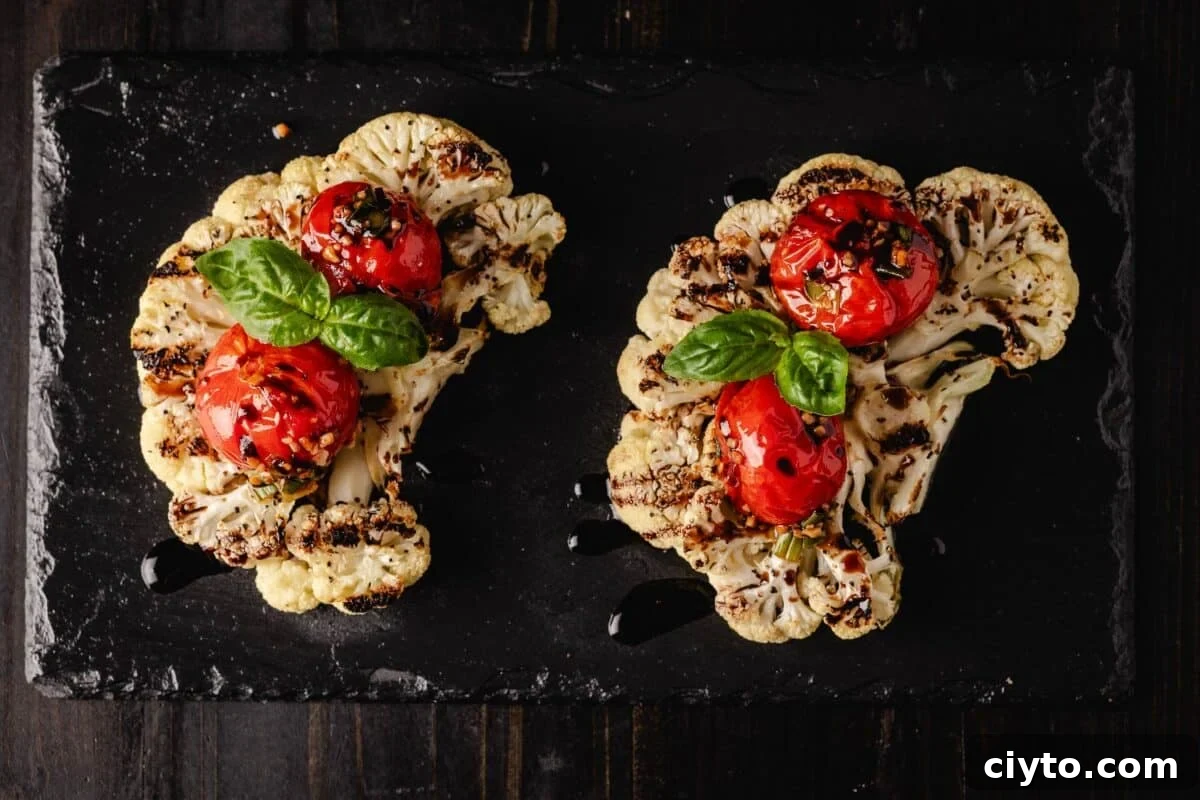 Cauliflower steaks on a black plate topped with tomatoes and basil leaves.