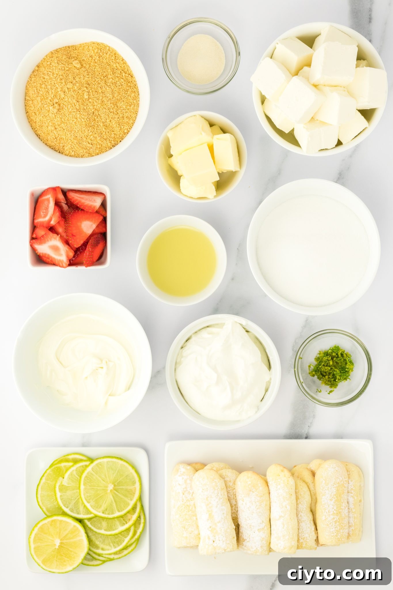 Ingredients for unbaked lime cheesecake recipe: graham cracker crumbs, butter, sugar, cream cheese, strawberries, gelatin, lime juice, whipped cream, white baking chocolate, lime zest, lady fingers, sliced lime, and sliced strawberries.