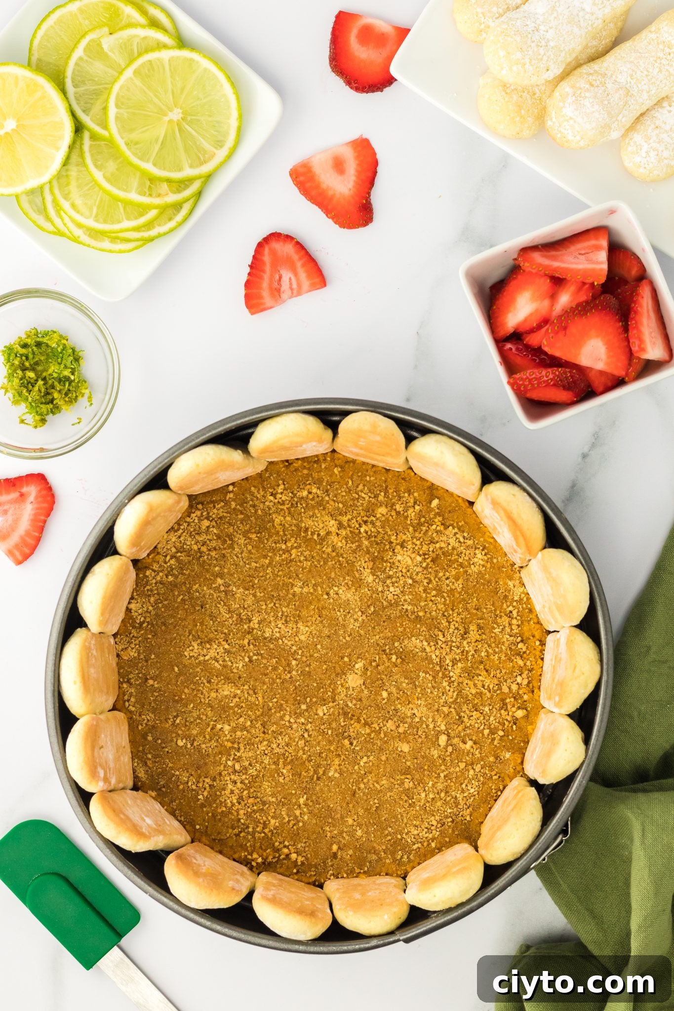 top down view of graham cracker crust formed in the bottom of a springform pan with ladyfingers around the edge.