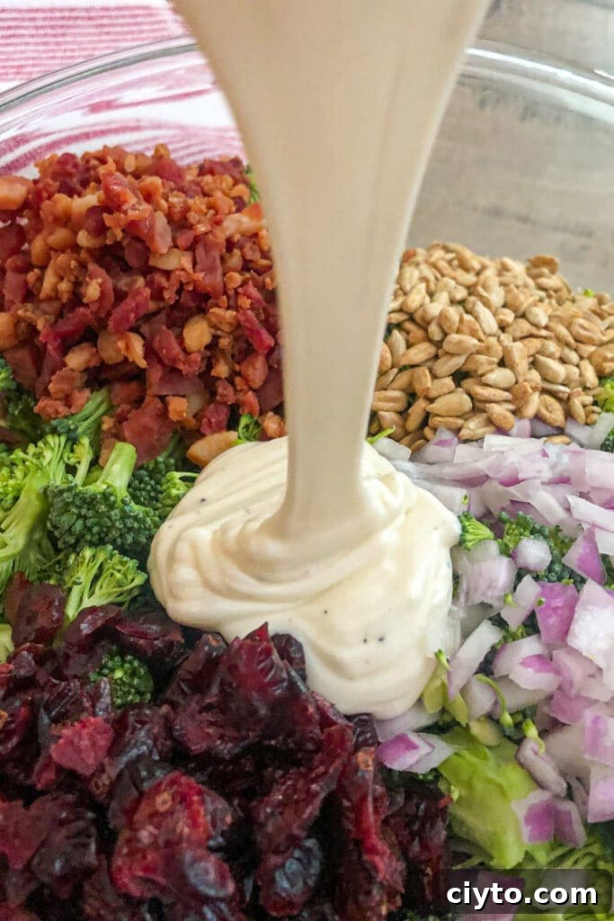 broccoli salad ingredients in a bowl with homemade dressing being poured over top