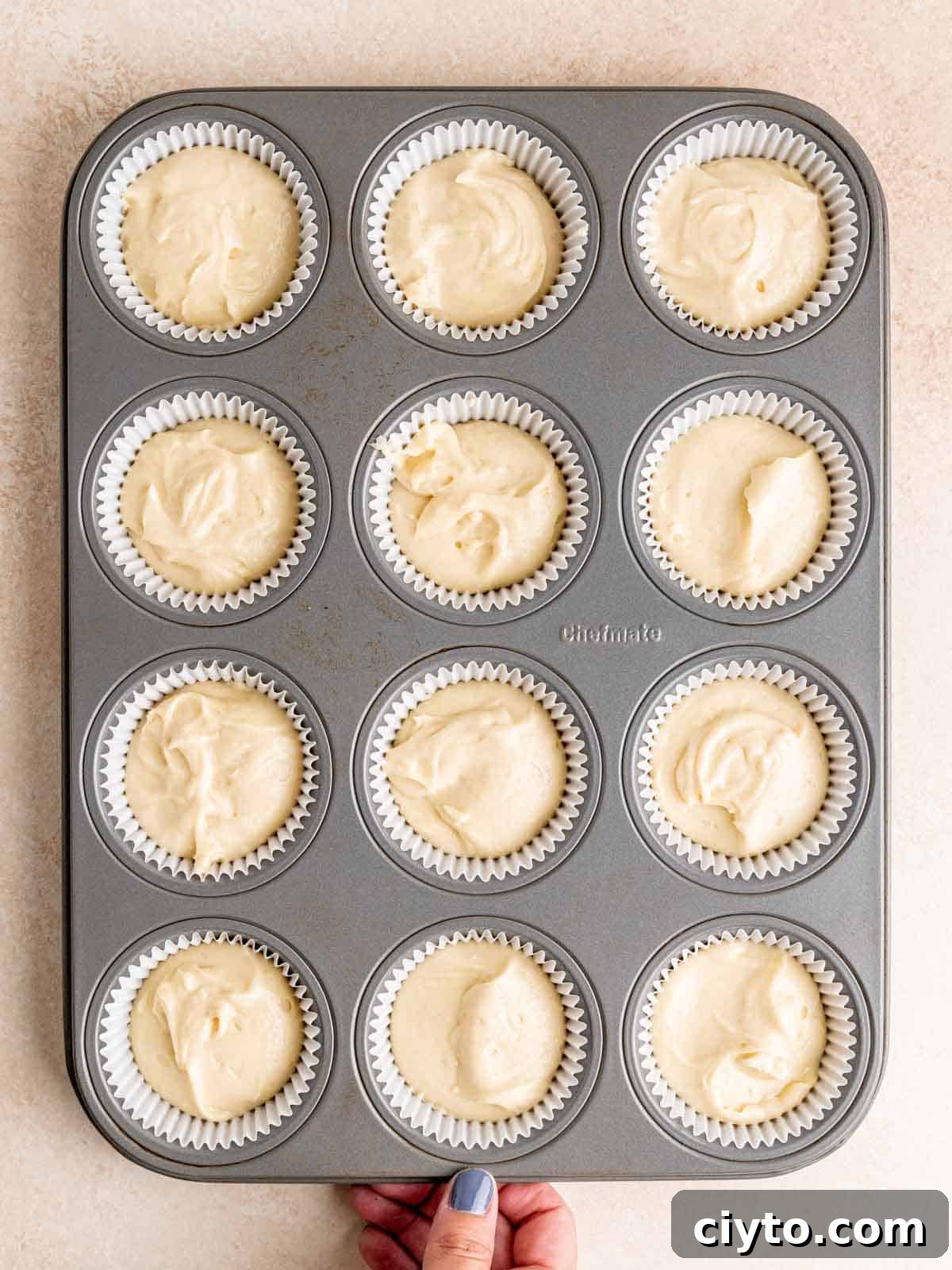 A muffin pan filled with liners full of almond cupcake batter.