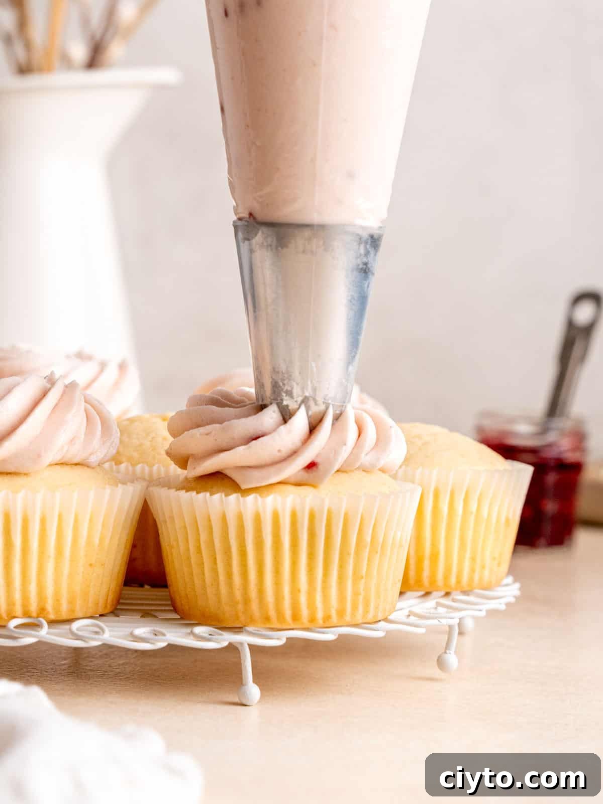 Piping raspberry jam frosting on top of almond cupcakes using a closed star piping tip.