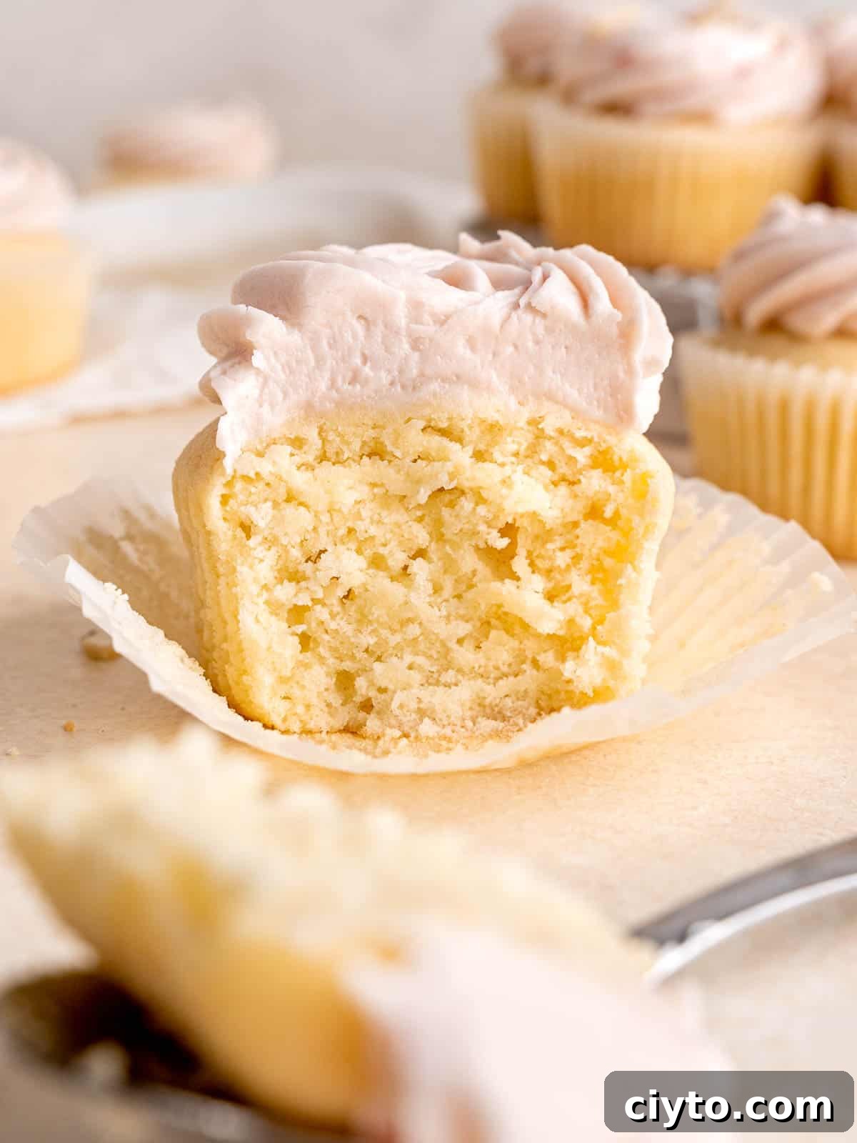 An almond cupcake with a bite taken out of it, showing its fluffy center.