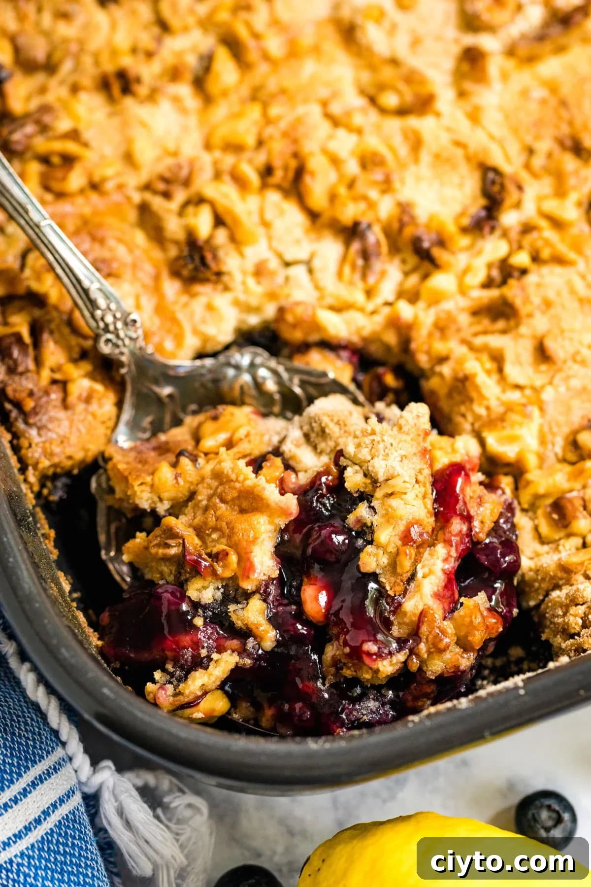 The corner of a pan of blueberry dump cake with a spoon in it revealing the berry mixture along with the crust.
