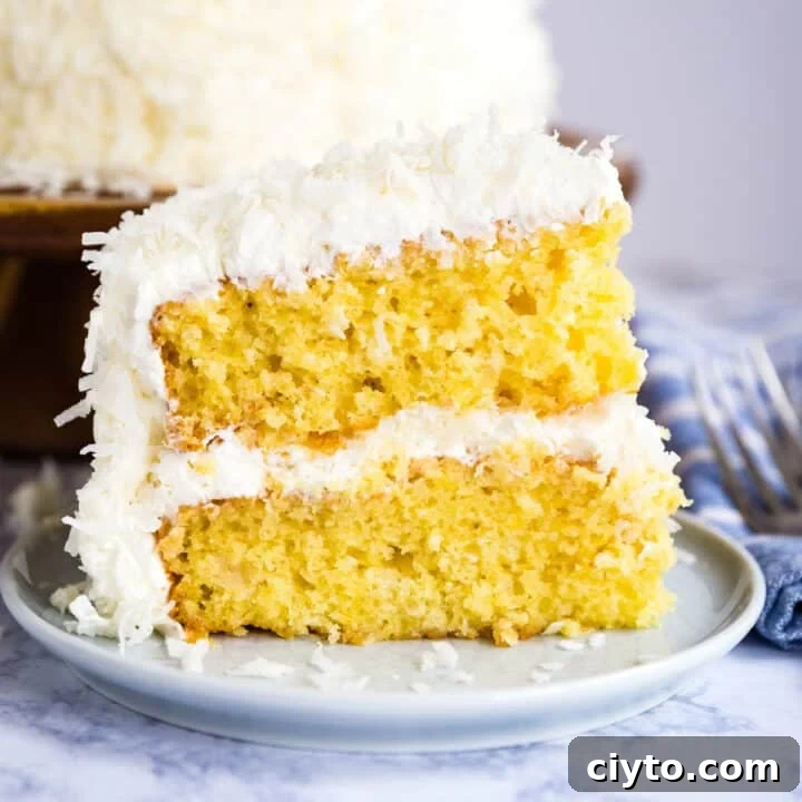 A slice of coconut cake on a plate with the full cake behind it.