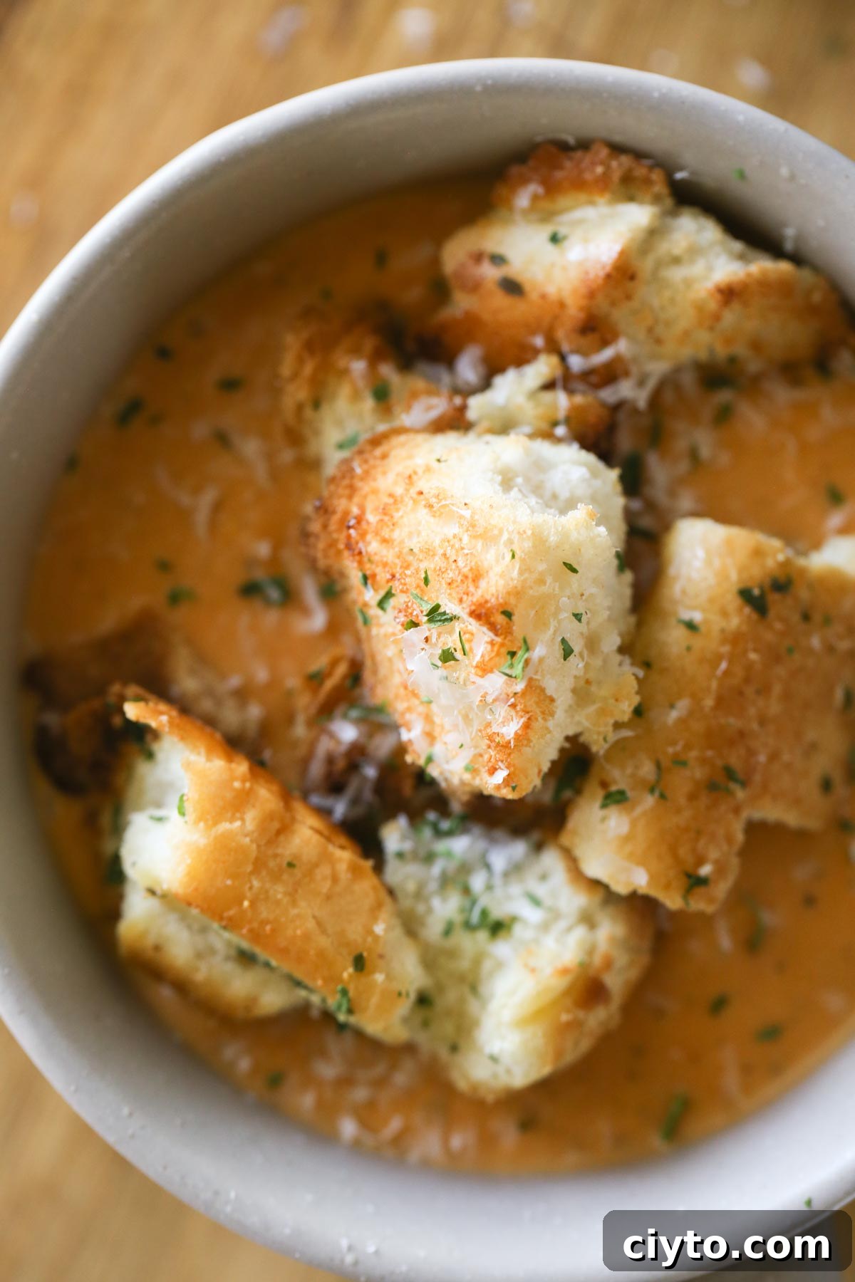 Overhead shot of a bowl of soup topped with Rustic Buttery Garlic Croutons and sprinkled with fresh Parmesan cheese.