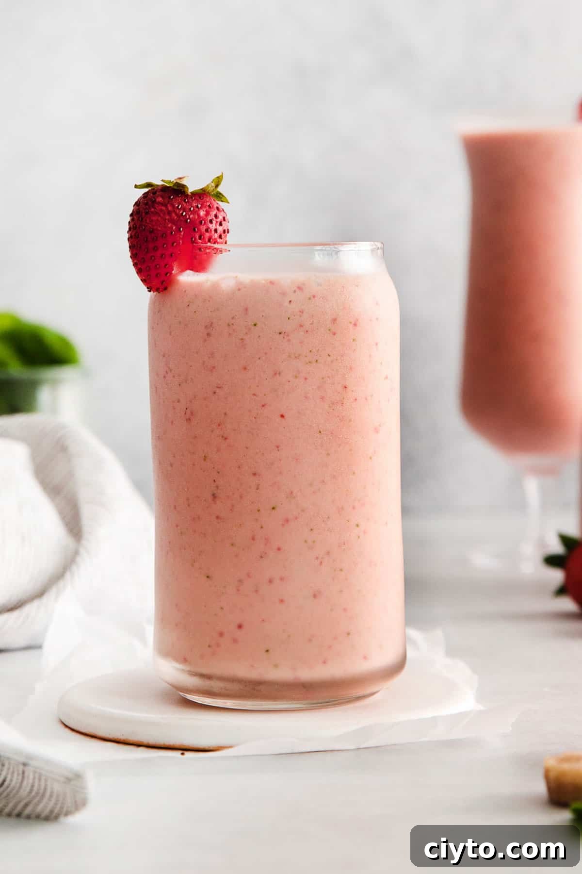 A close up of the strawberry spinach smoothie in a glass with a fresh strawberry on top