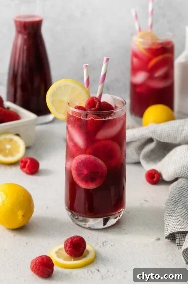 berry lemonade in a glass with two striped straws and a slice of lemon on the side