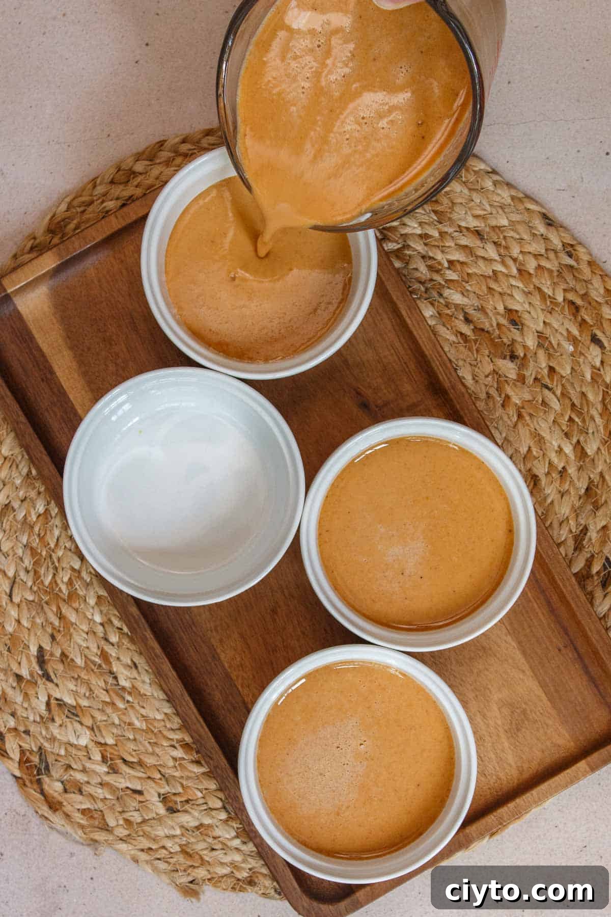 Uncooked custard being poured into individual ramekins.