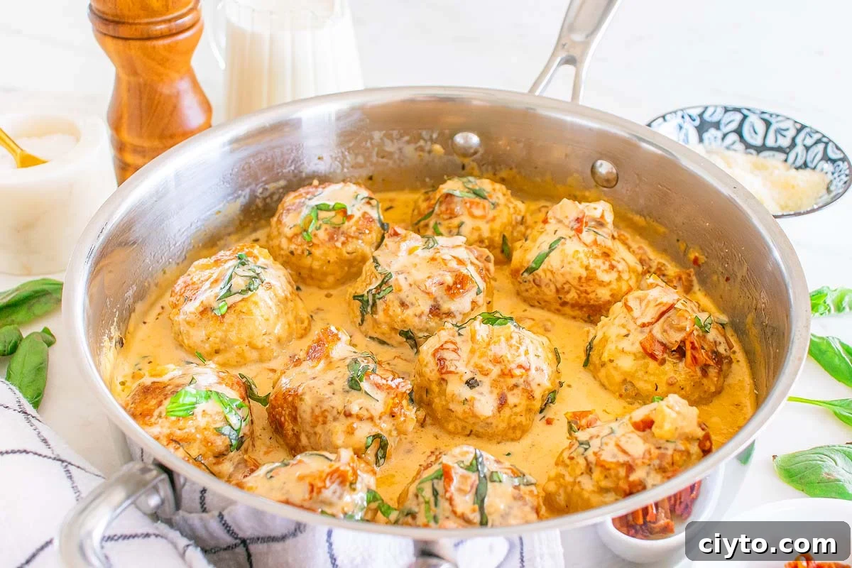 Marry me chicken meatballs in a creamy sauce garnished with herbs, cooked in a silver pan on a marble surface.