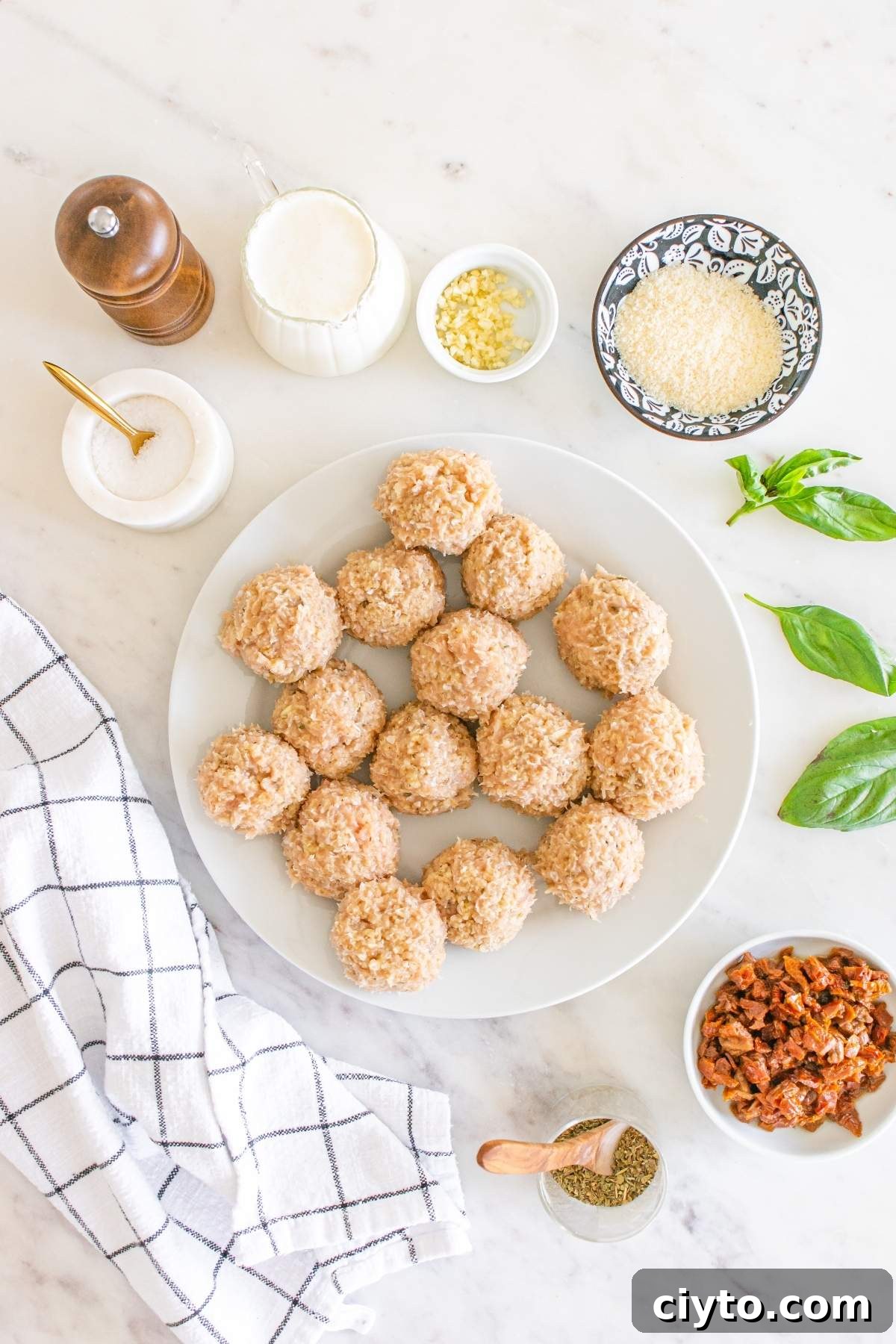 A plate of raw rice balls rests on a marble surface, hinting at a delicious transformation into "marry me" chicken meatballs. Surrounded by flavorful ingredients like salt, milk, garlic, breadcrumbs, basil, sundried tomatoes, and a checkered cloth, these are ready to enchant your senses.