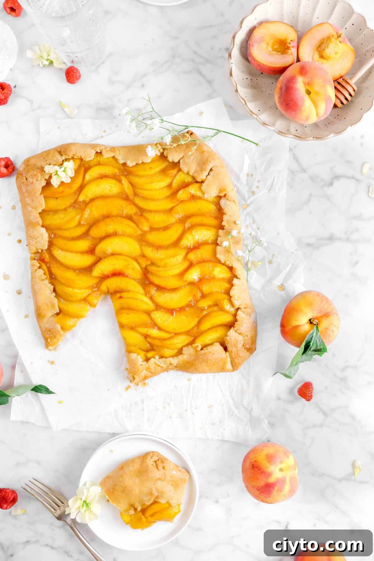 overhead shot of peach galette with slice on white plate, with flowers, and peaches around