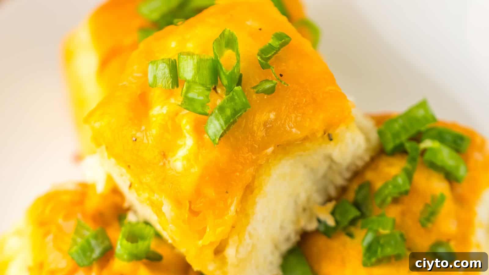 Close-up of cheesy garlic bread rolls topped with chopped green onions on a white plate, reminiscent of Loaded Buffalo Chicken Rolls.