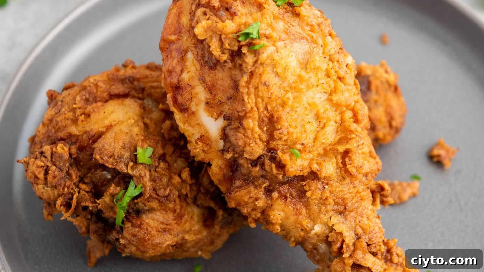 Two pieces of fried chicken on a gray plate, garnished with small bits of green herbs.